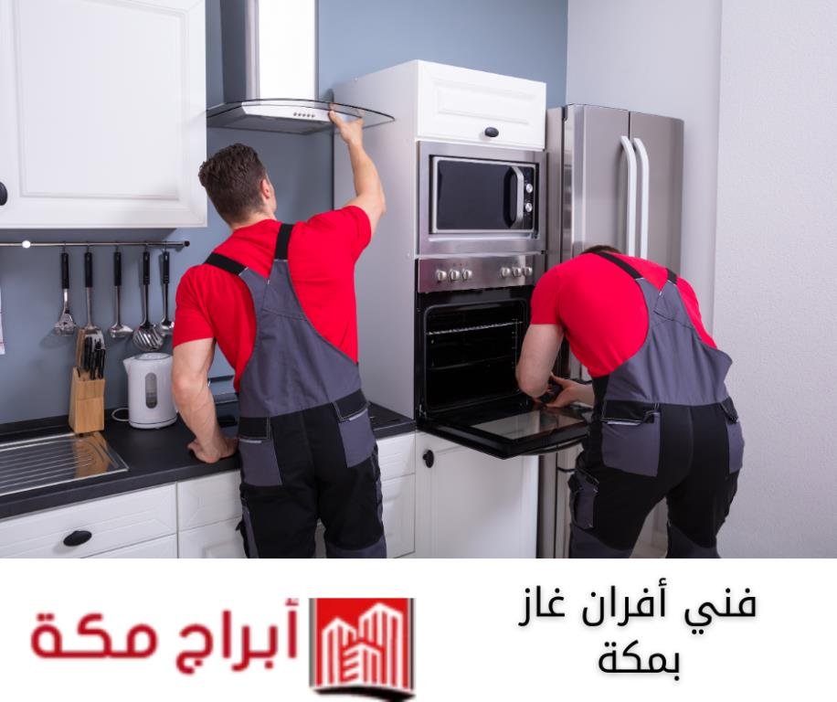 فني أفران غاز بمكة من شركة ابراج مكة يقوم بفحص وصيانة فرن غاز منزلي داخل مطبخ حديث، مع ارتداء زي العمل وشعار الشركة واضح.
